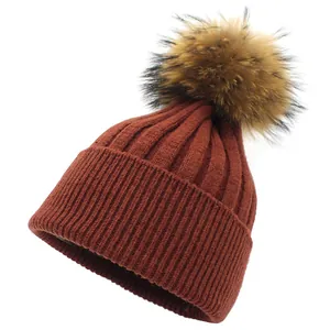 Detail view of burgundy knitted beanie with rib texture and fluffy faux fur pom-pom