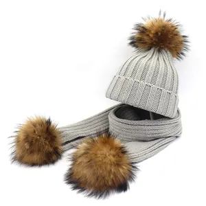 Detail showing the thick ribbed knit texture and fluffy faux fur pom-poms on the gray scarf