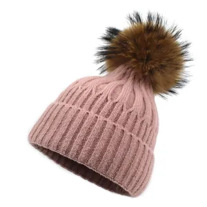Détail du bonnet en maille rose avec un grand pompon marron doux et texture côtelée