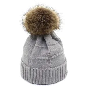 Close-up of light grey waffle knit beanie with fluffy faux fur pom-pom detail