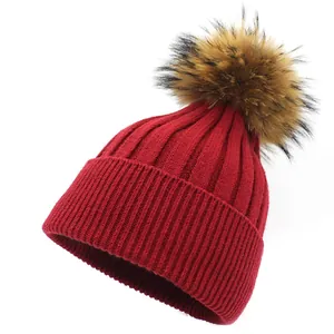 Detail view of dark red knit beanie with fluffy faux fur pompom and ribbed texture