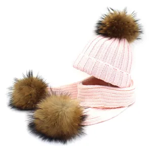 Pink winter knit set featuring a beanie hat and scarf with large brown faux fur pom poms