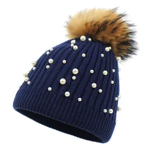 Detailed knit texture of navy wool hat featuring white pearl beads and faux fur pom-pom