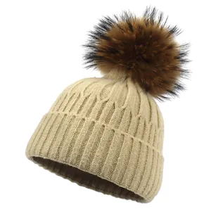 Détail du bonnet en maille côtelée beige avec pompon en fausse fourrure marron duveteuse