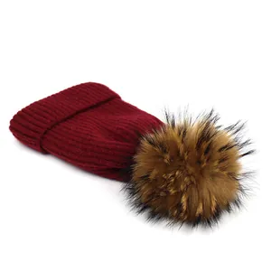 Detail showing Burgundy ribbed knit texture and large raccoon fur pom-pom on winter hat