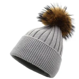 Close-up of light grey striped knit beanie with fluffy brown pom-pom and rolled cuff