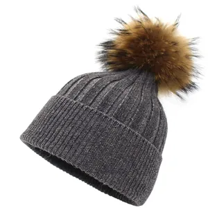 Close-up of gray rib-knit beanie with fluffy raccoon fur pom-pom and warm folded brim