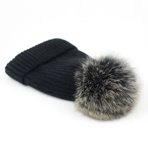 Detalle de gorro de punto negro con pompón de pelo sintético y textura de canalé suave