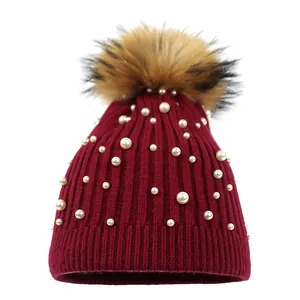 Burgundy knitted winter hat with pearls and a fluffy brown faux fur pom pom