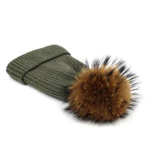 Close-up of olive green ribbed knit beanie with a fluffy raccoon fur pompom detail