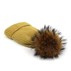 Detail of mustard yellow ribbed knit beanie with large fluffy raccoon fur pom-pom topper