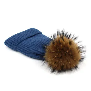 Detailed view of dark blue ribbed knit hat with large brown fluffy fur pompom on top