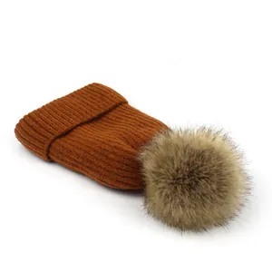 Detail van de karamelgekleurde gebreide muts met ribstructuur en zachte pompon