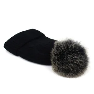 Detalle del gorro de punto acanalado negro con un pompón de piel de zorro real suave