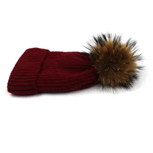 Burgundy wool knit beanie with large fluffy raccoon fur pompom for winter warmth