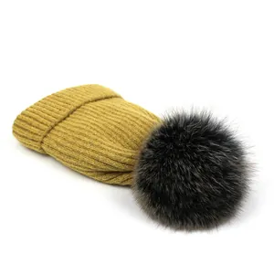 Detalle de gorro de punto amarillo mostaza con pompón de piel de zorro real suave