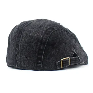 Detail of washed black denim beret featuring a bronze metal buckle and side embroidery