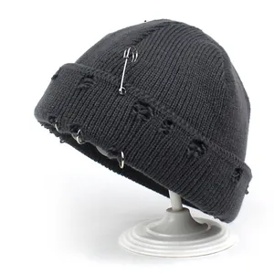 Dark grey knitted beanie featuring distressed details with metal rings and safety pin