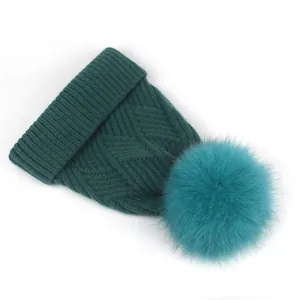 Makroansicht der dunkelgrünen Strickmütze mit Zopfmuster und flauschigem Pelzbommel