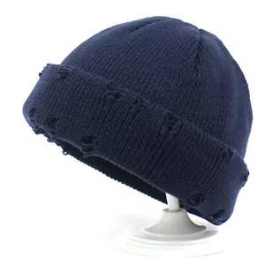 Dettaglio del berretto in maglia blu scuro con fori usurati e trama a coste su supporto
