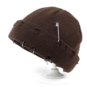 Close-up of brown distressed knit beanie featuring silver metal rings and safety pin detail