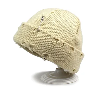 Close-up of beige knit beanie featuring metal rings and decorative safety pin accents
