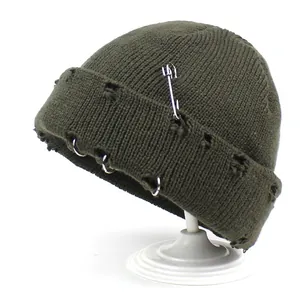 Detail of dark green distressed knit beanie with silver rings and a safety pin accent