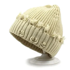 Detail of cream ribbed knit beanie with distressed fringe edge on white background