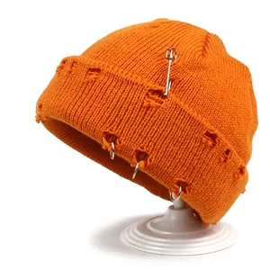Detail of orange distressed knit beanie with silver metal rings and safety pin accessory