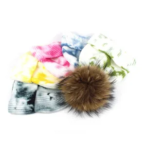 Five assorted tie-dye ribbed knit beanies with large fluffy faux fur pom poms on top