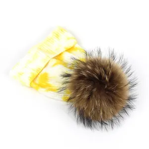 Tie-dye yellow and white knit beanie with a fluffy brown pompom for winter warmth