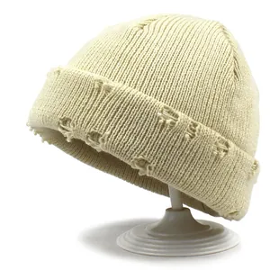 Dettaglio del berretto in maglia bianco sporco con bordi strappati e texture in lana