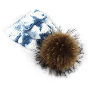 Detail of blue and white tie-dye knit beanie featuring a large fluffy brown fur pom-pom