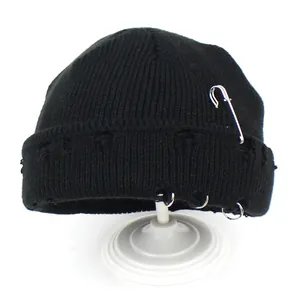 Detail of black knit beanie with punk metal rings, silver safety pin and distressed edges