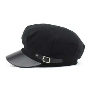 Detail view of black wool newsboy hat with textured faux leather brim and metal buckle