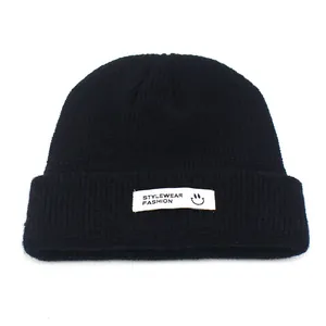 Detail einer schwarzen Strickmütze mit weißem gewebtem Aufnäher mit Smiley und Logo