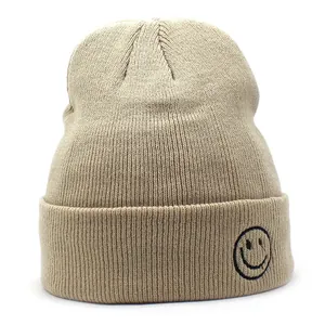 Dettaglio del berretto in maglia beige con ricamo a forma di faccina sorridente nera