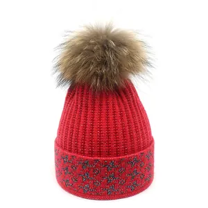 Detailed view of red knit beanie featuring silver star patterns and a fluffy faux fur pompom