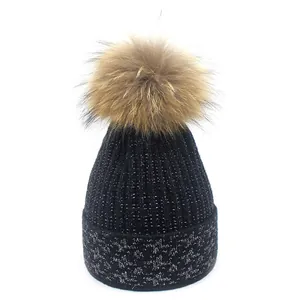 Close-up of black knit beanie with silver tinsel details and a fluffy brown pompom