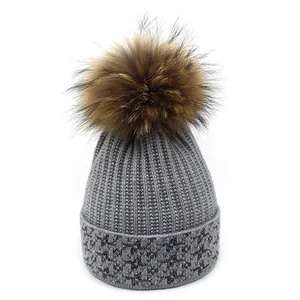 Detail of grey knitted winter beanie featuring star patterns and a fluffy fur pom-pom