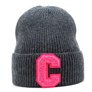 Detail of grey knitted beanie with a large pink letter C embroidery patch on the front cuff