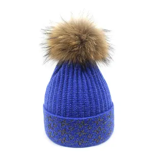 Close-up of royal blue knit beanie featuring sparkling silver thread and faux fur pom-pom