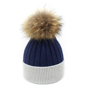 Détail du bonnet en maille bicolore bleu et gris avec un grand pompon en fausse fourrure