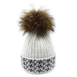Detailed view of white ribbed knit beanie with brown fur pom-pom and star pattern