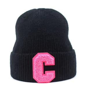 Detail of black ribbed knit beanie featuring a pink bouclé embroidered letter C patch