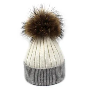 Détail du bonnet en tricot bicolore avec un grand pompon en fourrure marron duveteux