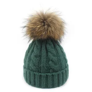 Detalle de punto grueso y pompón de piel grande en gorro de lana verde oscuro