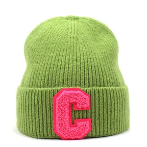 Detail of green ribbed knit beanie featuring pink C towel embroidery patch