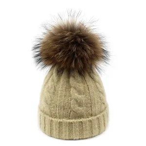 Detalle del gorro de invierno beige con textura de punto de ochos y pompón de piel sintética