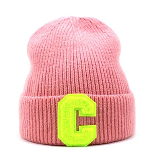 Detail of pink ribbed knit beanie featuring a fluorescent yellow letter C patch